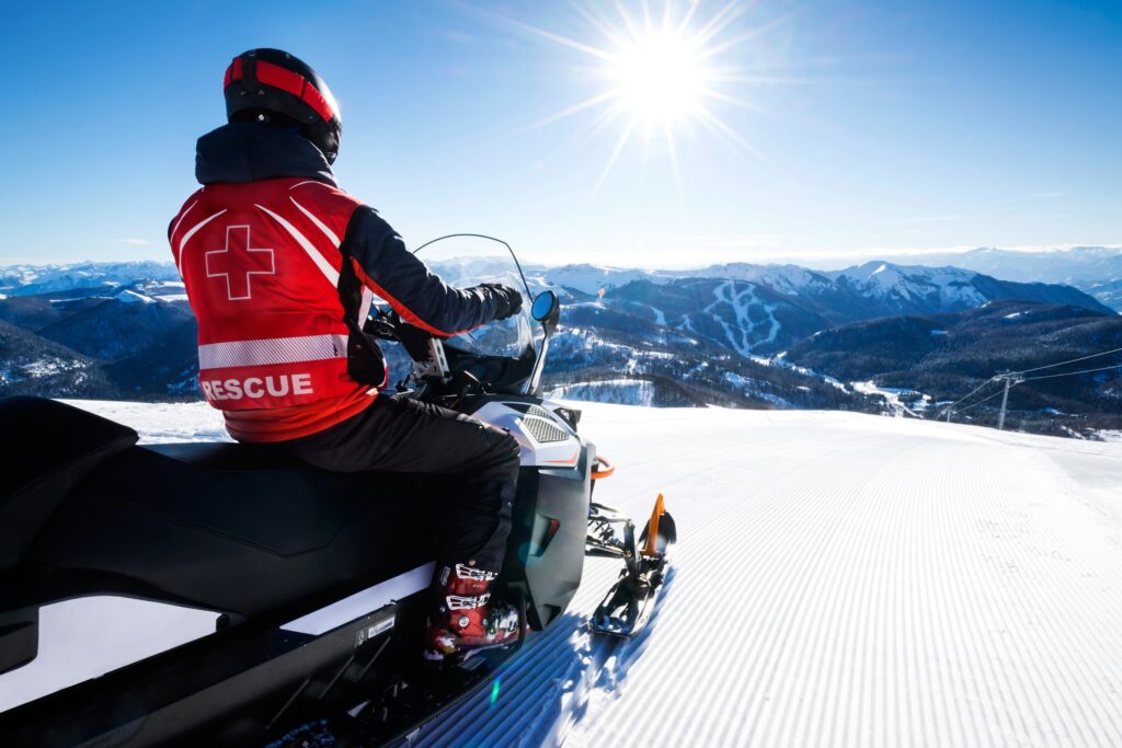 First responder on a sunny blue sky day enjoying a snow-caped mountain ridge while sitting on their two seater snowmobile.